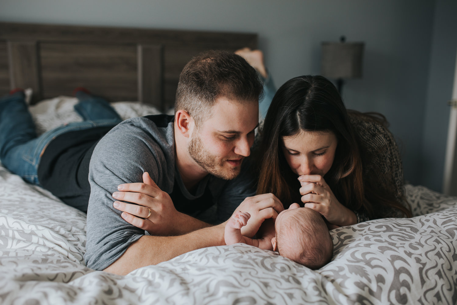 husband and wife lying on bed with 6 week old baby girl between them - Markham lifestyle photos