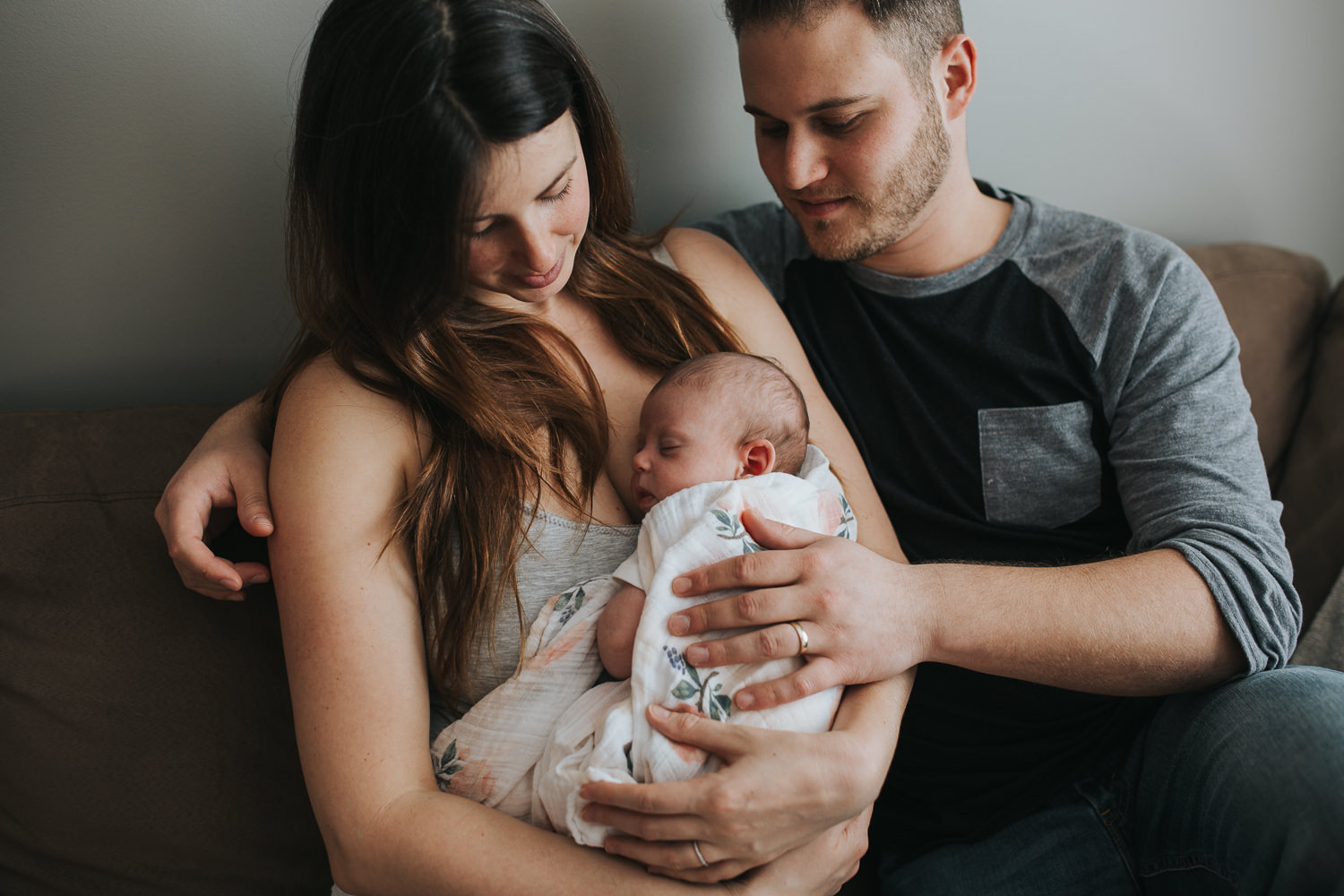 new parents sitting on couch holding and looking at 6 week old baby girl - Stouffville in-home photos