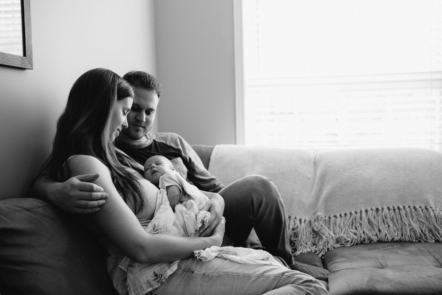 new parents sitting on couch holding and looking at 6 week old baby girl - Markham in-home photos