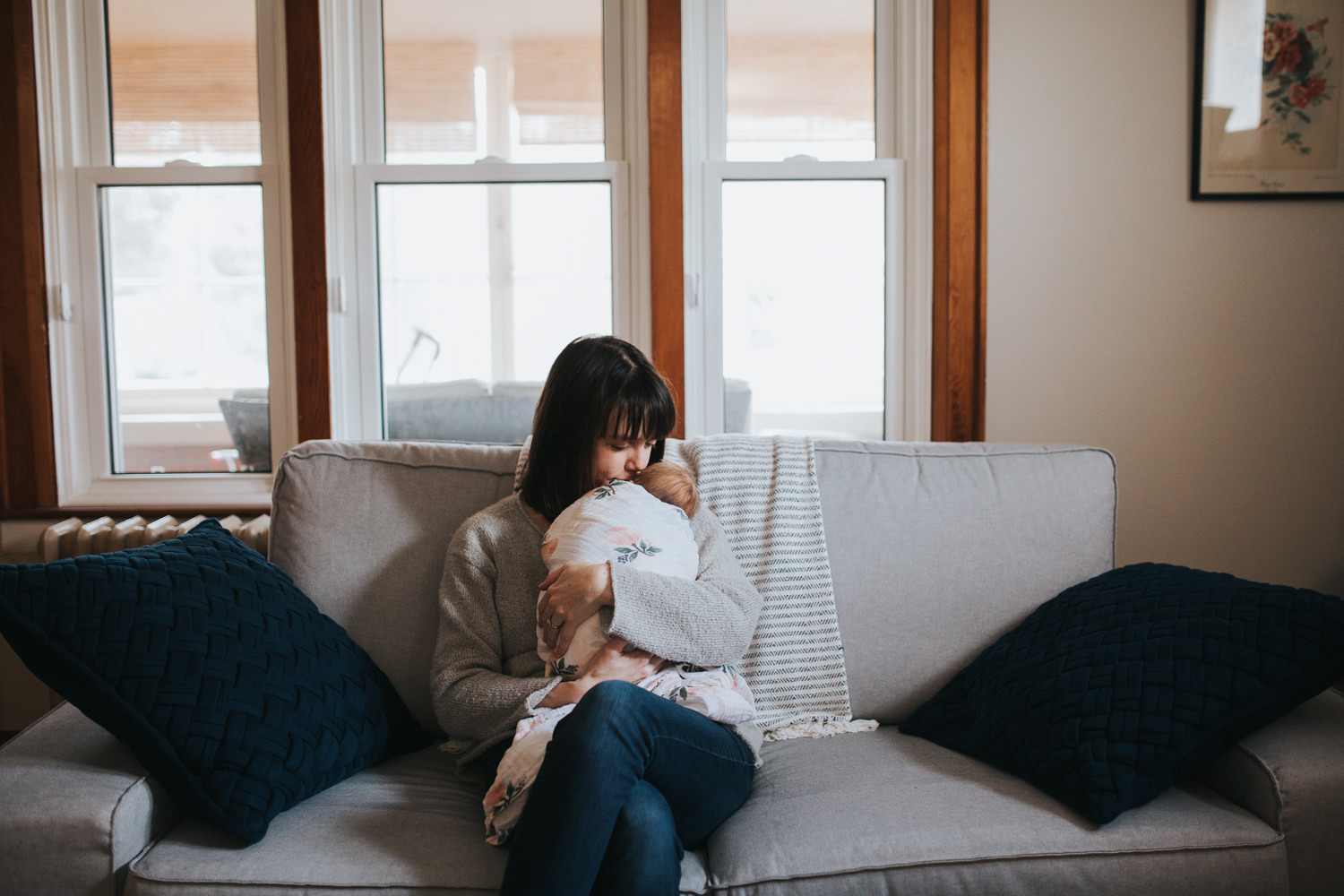 brunette mother holds 5 week old swaddled, sleeping baby girl while sitting on couch - Markham lifestyle photography