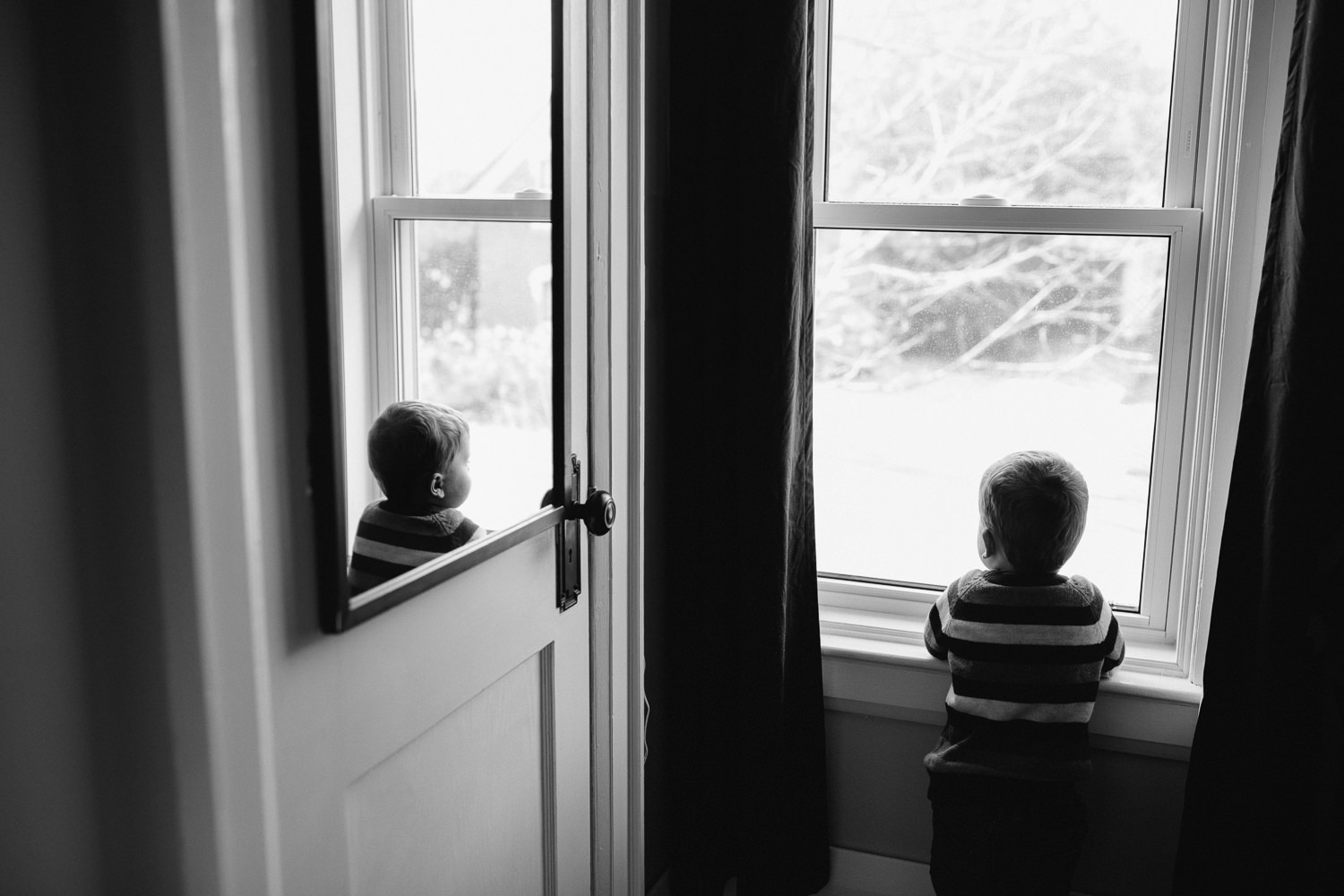 3 year old toddler boy looks out window, can see reflection in mirror - Markham in-home photos