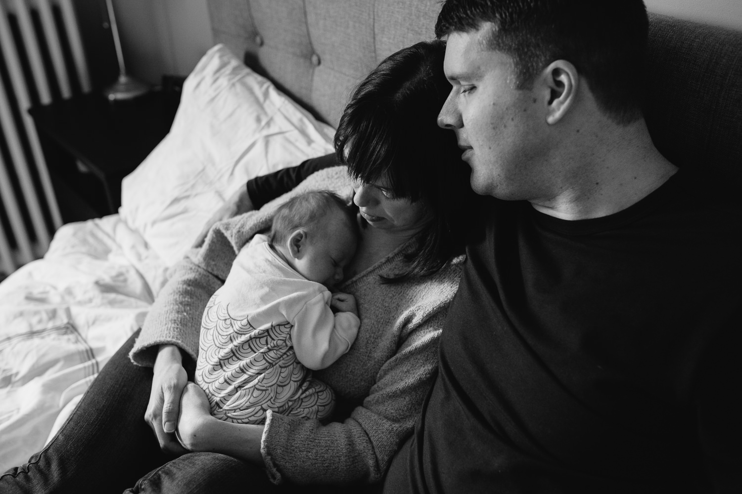 husband and wife snuggle on bed, mom holds 5 week old baby girl - Stouffville in-home photography