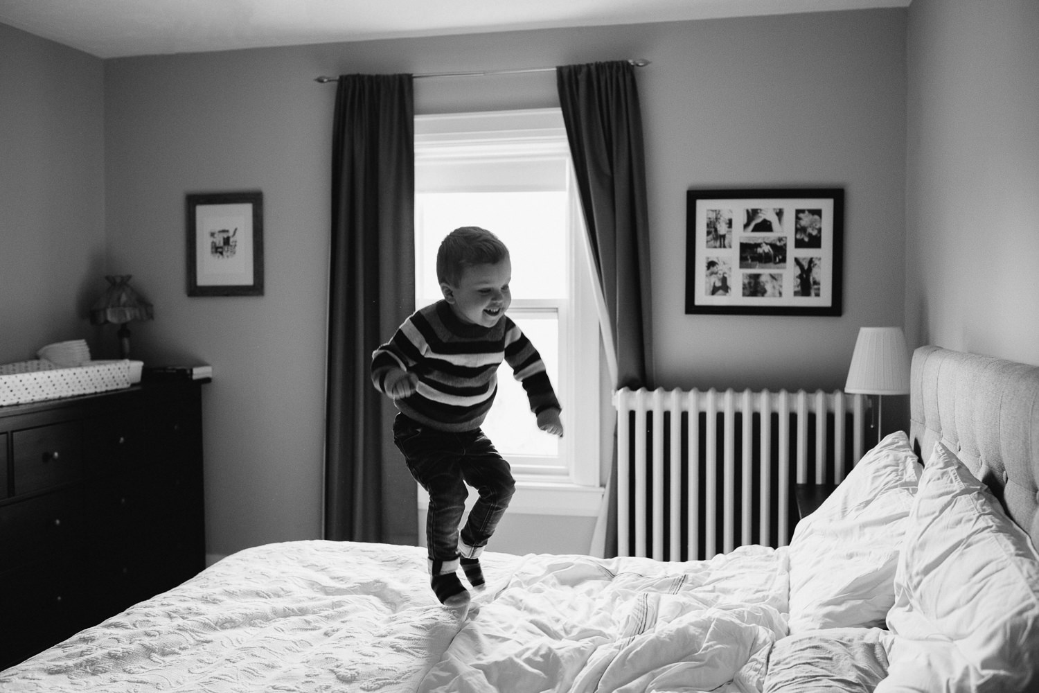 3 year old toddler boy in striped sweater jumps on parent's bed - Markham in-home photography