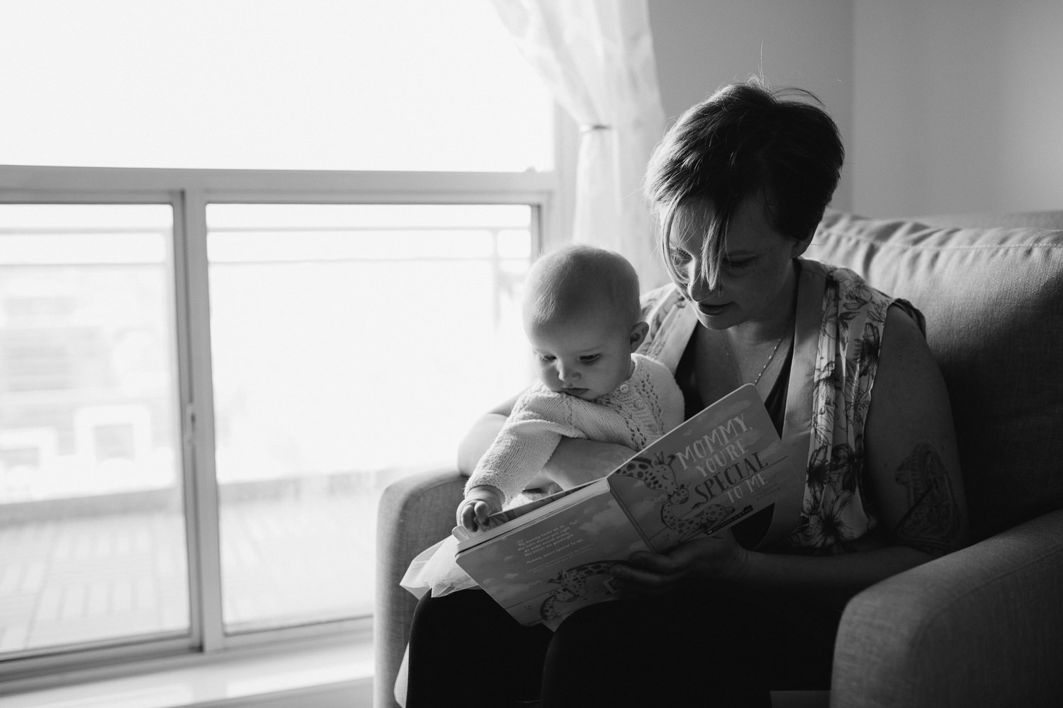 mom sitting in rocking chair reading book to 5 month old baby girl - Newmarket in-home photography