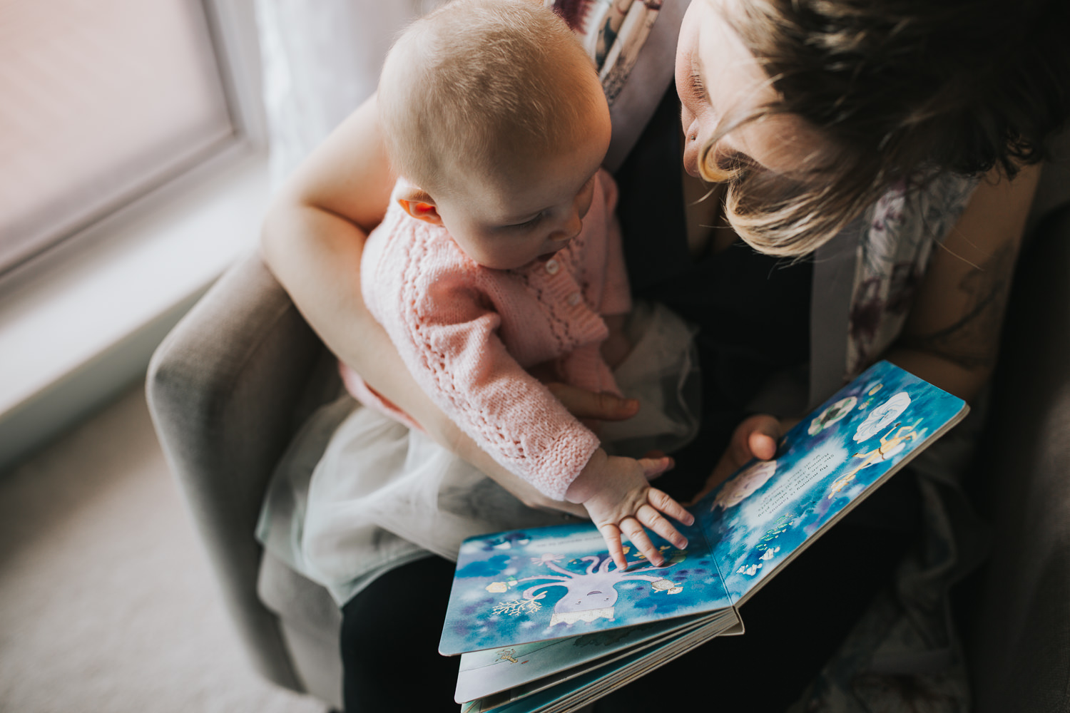 mom sitting in rocking chair reading book to 5 month old baby girl - Stouffville in-home photography