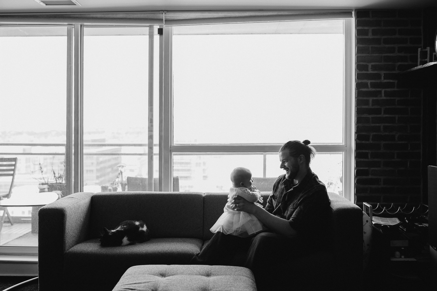 5 month old baby girl in pink sweater sitting on father's lap while they play on couch - Stouffville in-home photos