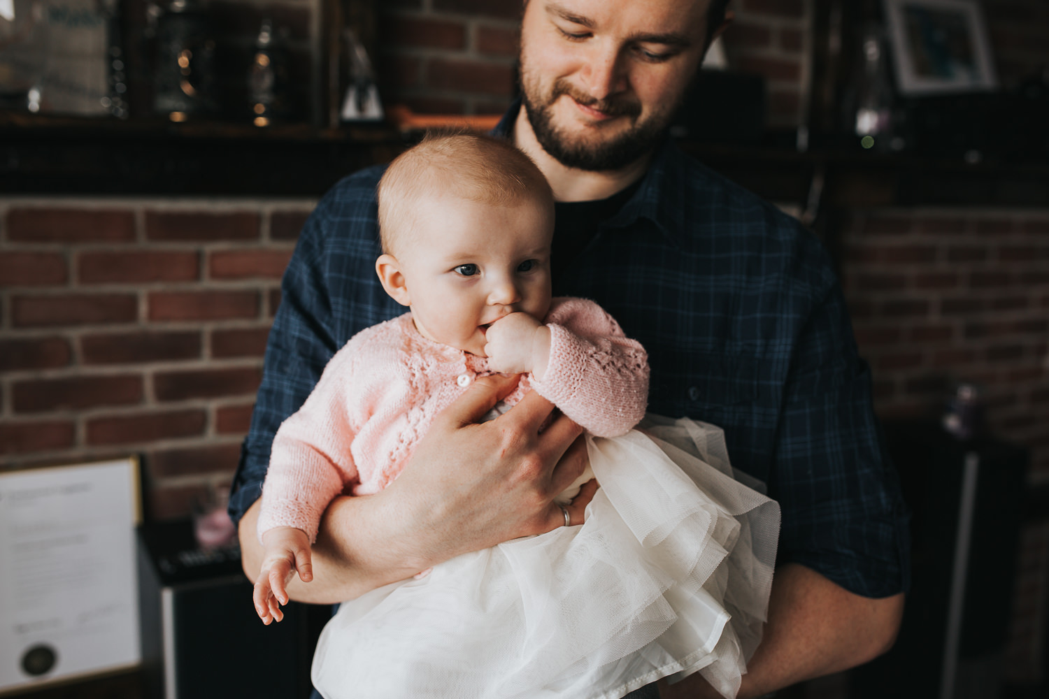 dad holds 5 month old baby girl in pink sweater who is chewing on her hands - Barrie lifestyle photography