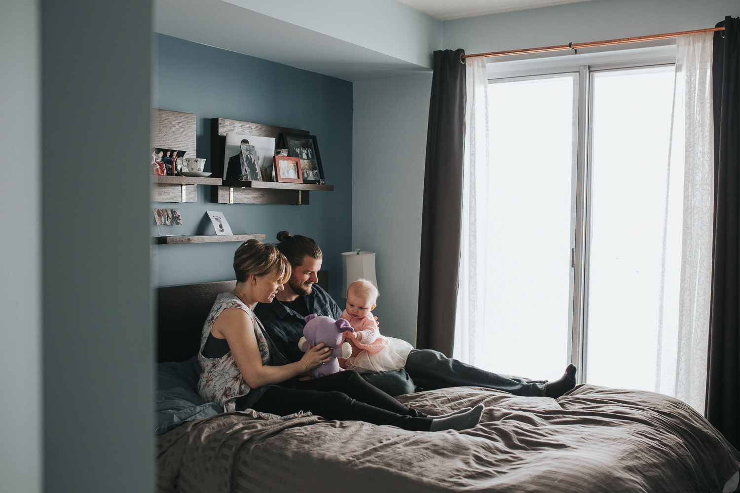 parents sitting on master bed holding and playing with 5 month old baby girl in pink sweater and tutu - Stouffville in-home photos