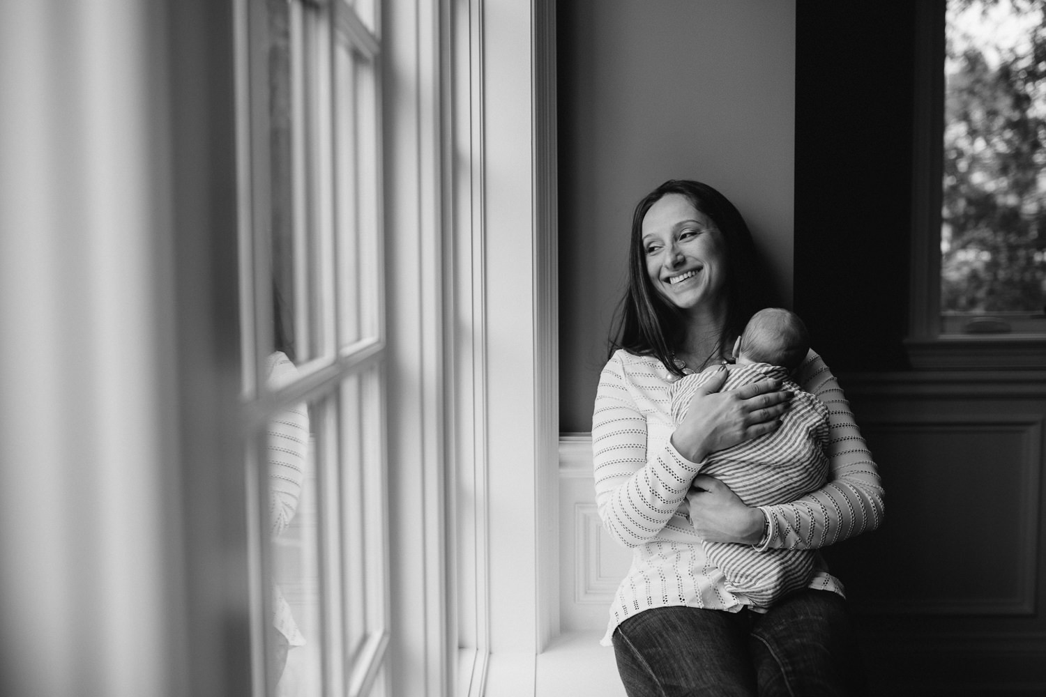 mother sitting on window seat holding 2 week old baby son against chest - Markham lifestyle photos