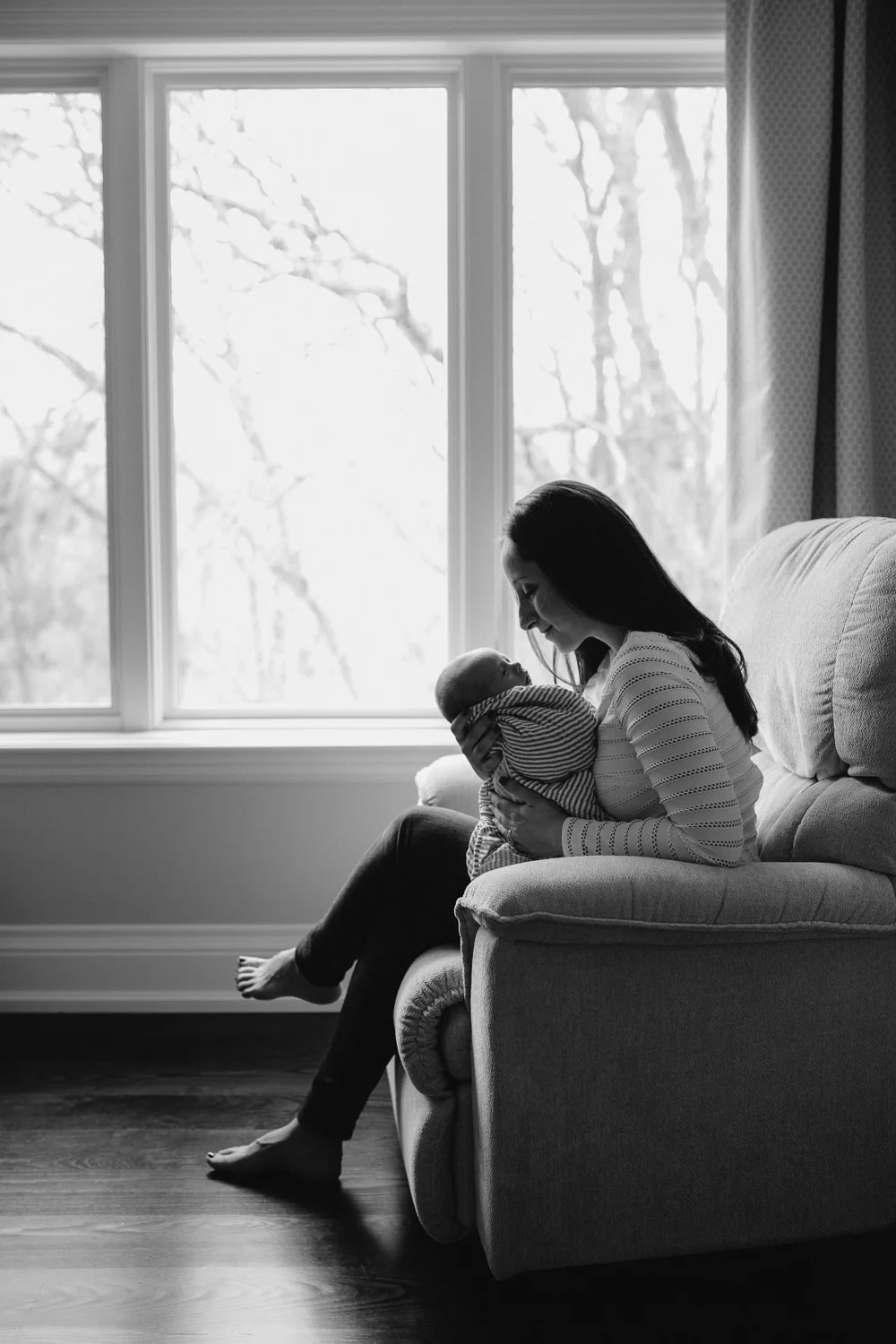 mom sitting in glider holding and looking at 2 week old baby boy - Barrie in-home photos