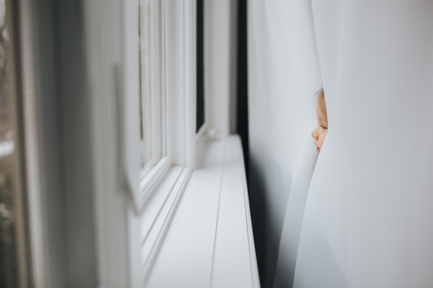 2 year old toddler girl's face peeking through curtains - Barrie lifestyle photography