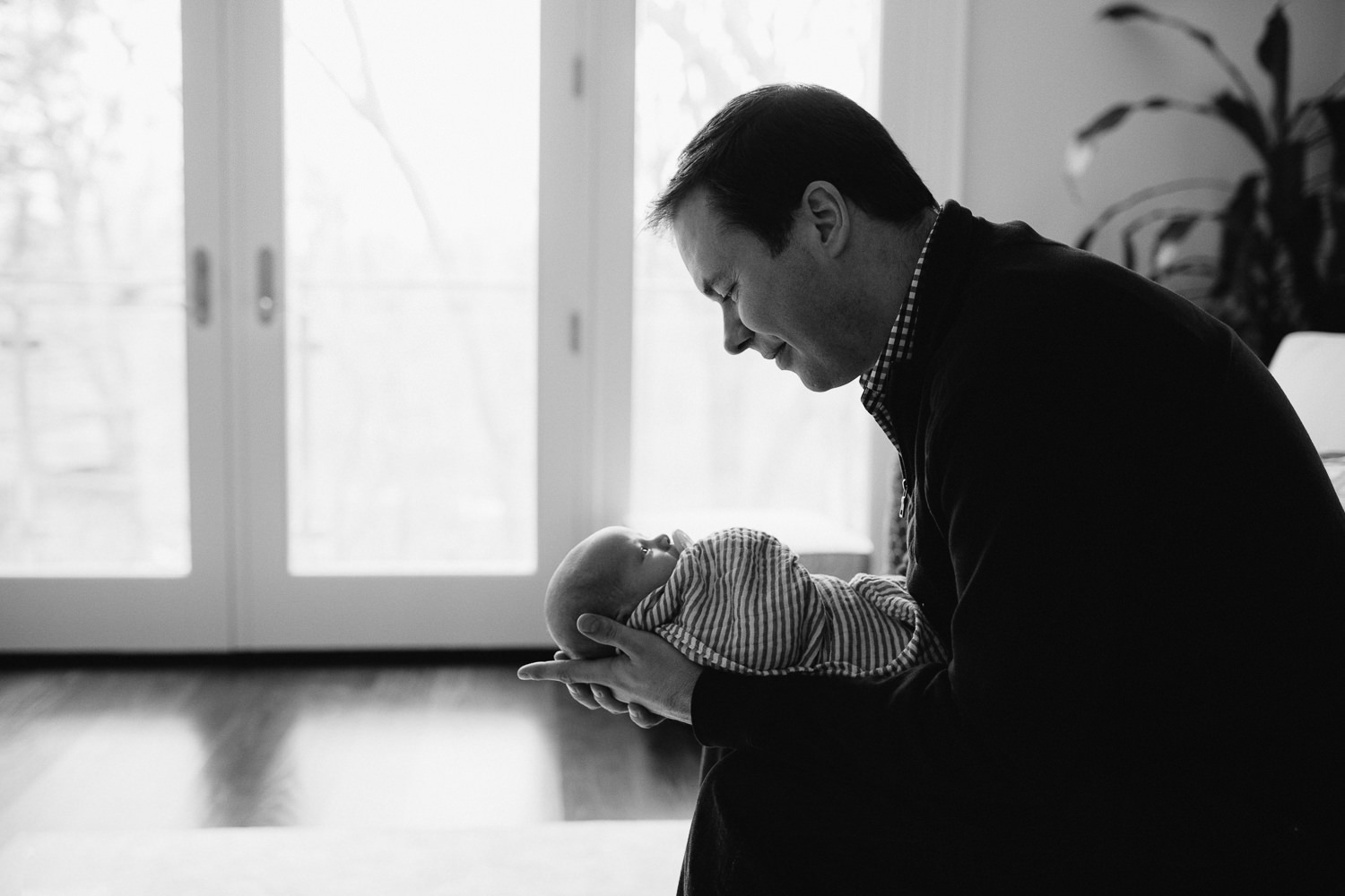 dad leaning forward, holding and looking at 2 week old baby boy - Markham lifestyle photos