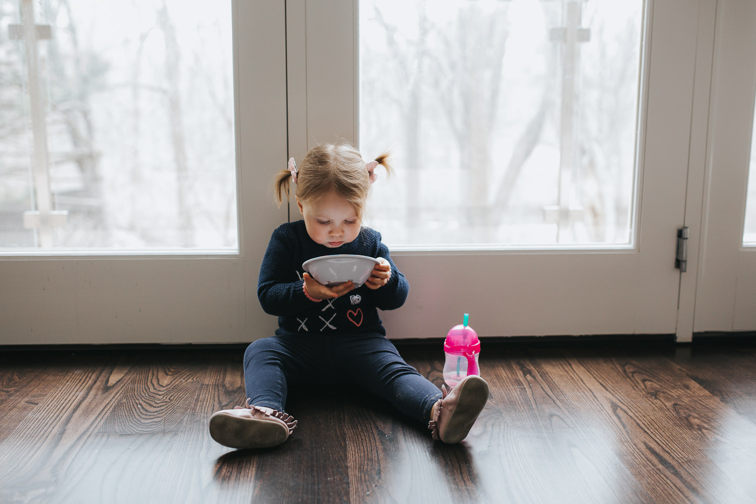 2 year old toddler girl with pigtails sitting on floor eating snack from a bowl - Newmarket lifestyle photos