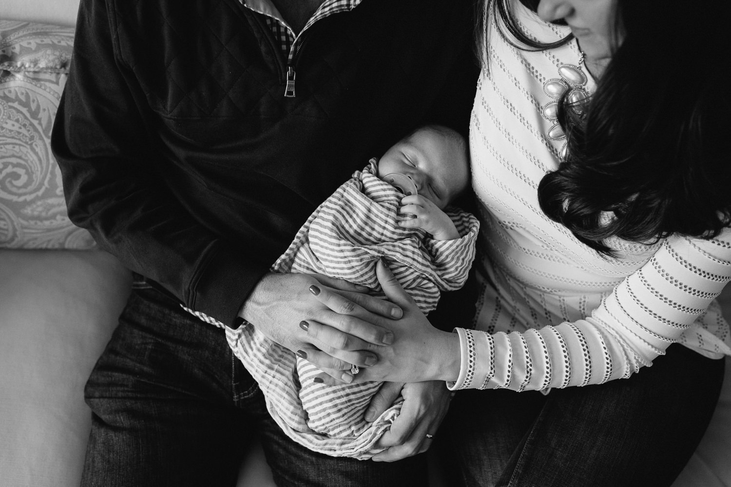 husband and wife hold hands while snuggling 2 week old baby son - Markham in-home photos