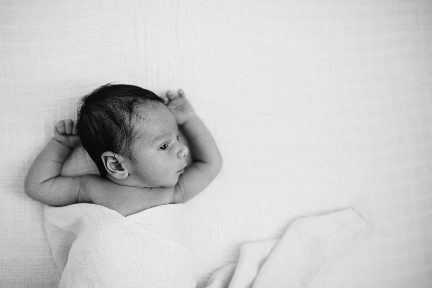 2 week old baby boy in diaper lying awake with arms in air - Uxbridge Lifestyle Photography 
