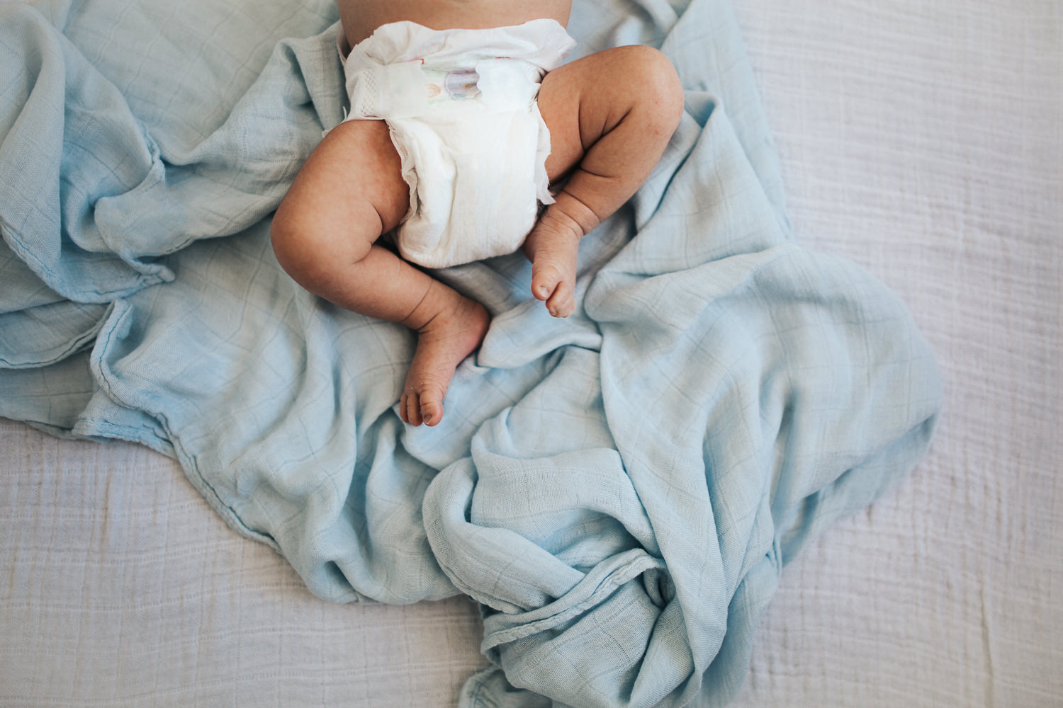 2 week old baby boy legs and feet lying on blue swaddle in diaper - Newmarket in-home photography