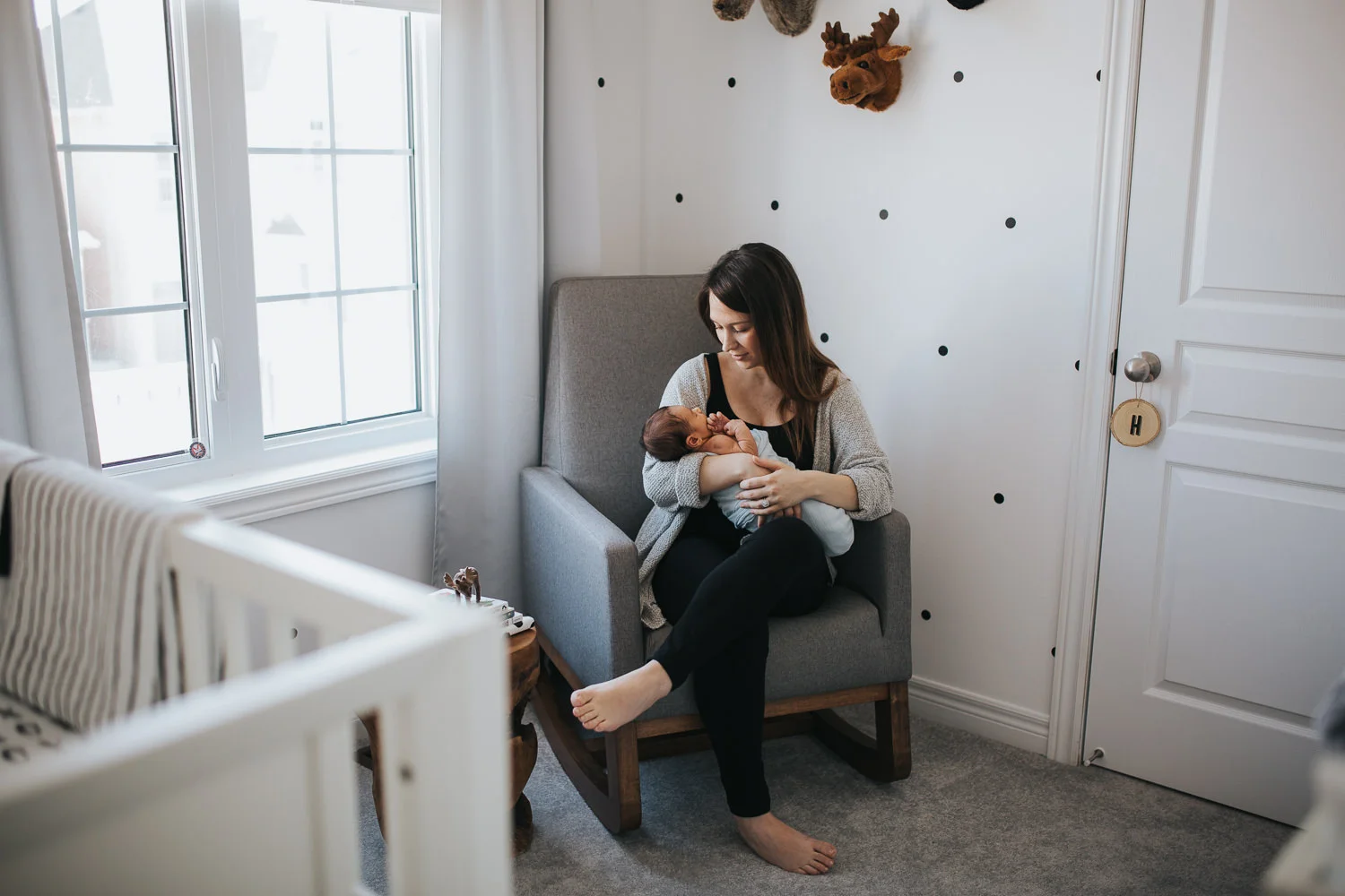 new mom sitting in rocking chair holding 2 week old baby boy, looking at him - Markham In-Home Photography
