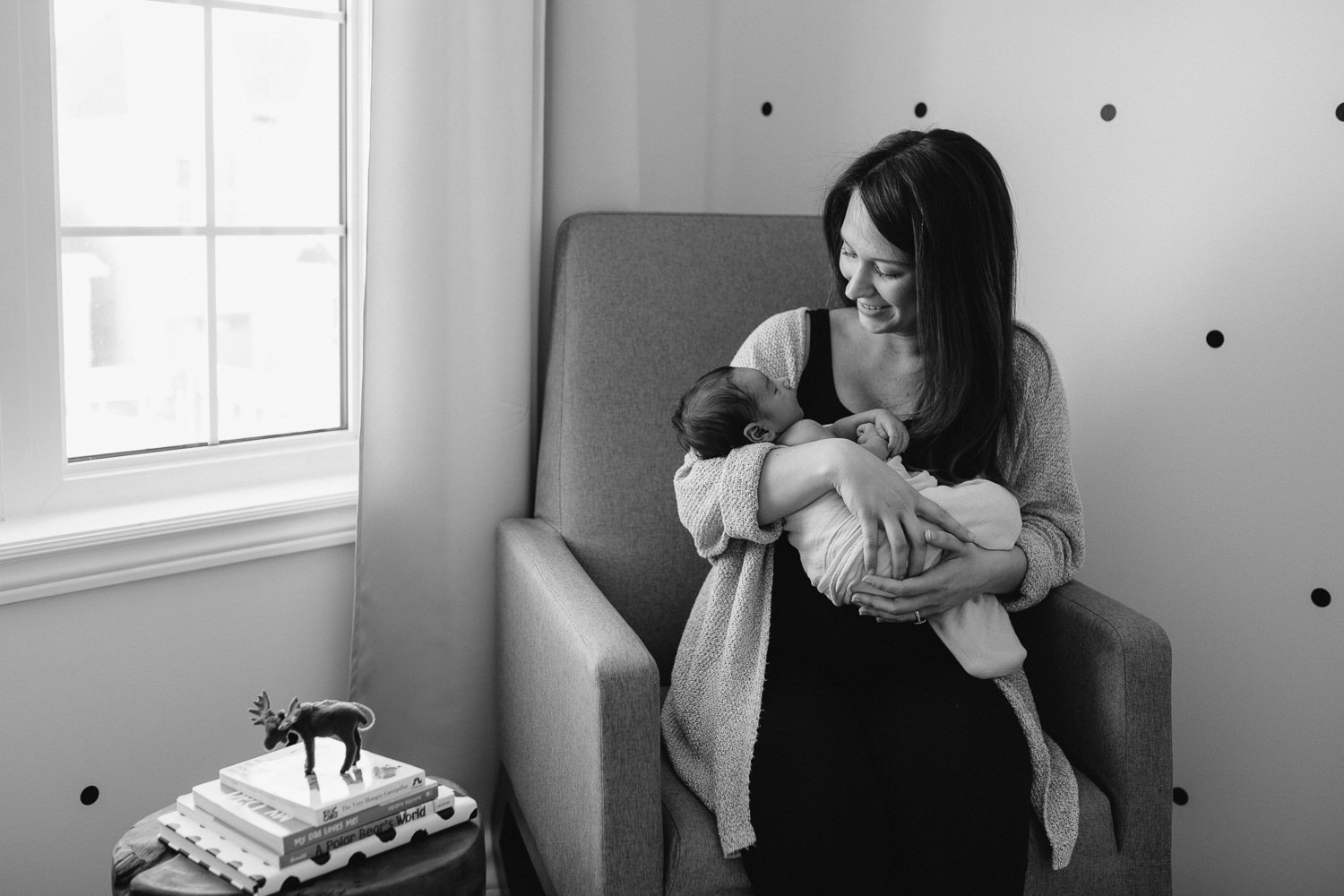 new mom sitting in rocking chair holding 2 week old baby boy, looking at him - Markham Lifestyle Photography 