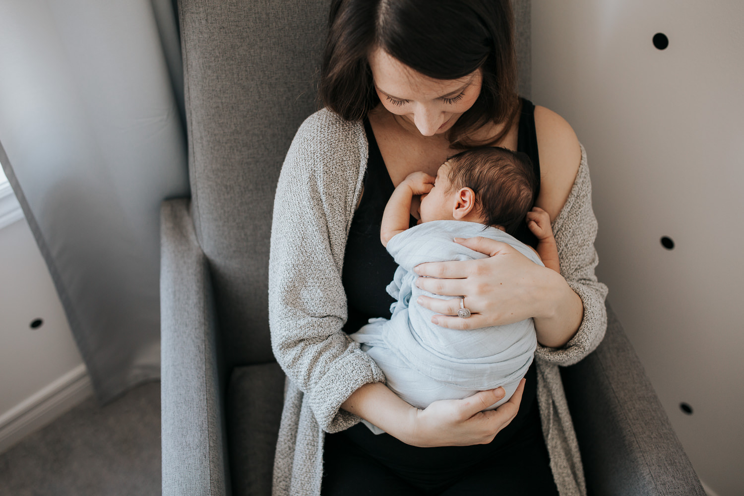 brunette mother holding sleeping 2 week old baby boy on chest in rocking chair - Barrie In-Home Photography