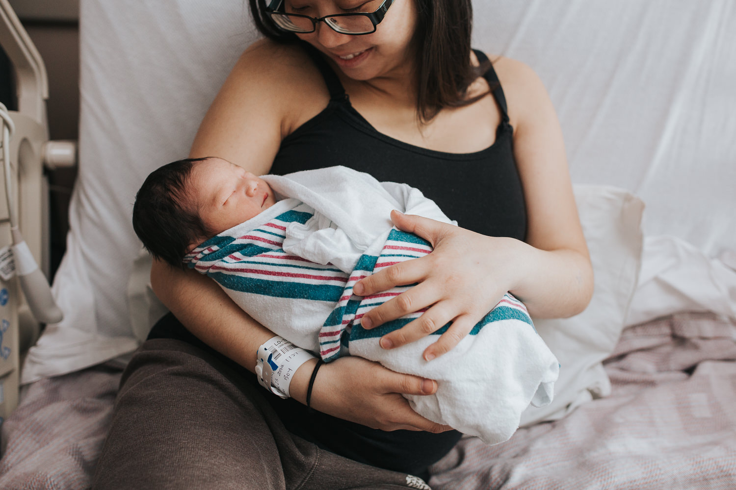 new mom sitting in hospital bed holding and looking at newborn baby son - Uxbridge Fresh 48 Photography