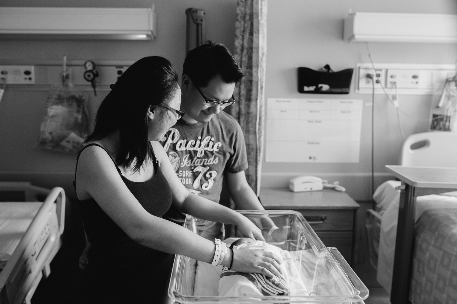 brand new parents looking at 1 day old baby boy lying in hospital bassinet - Barrie Fresh 48 Photography