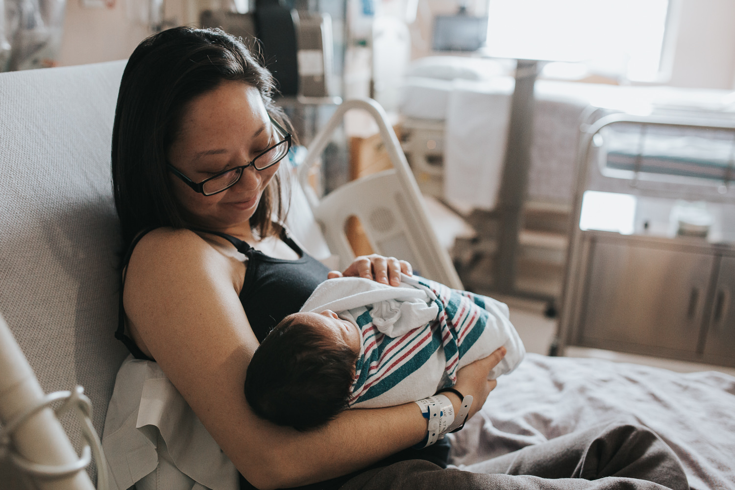 new mom sitting in hospital bed holding and smiling at newborn baby boy - Newmarket Fresh 48 Photos