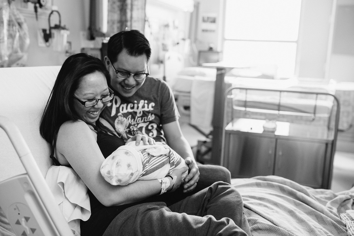 new parents sitting in hospital bed holding and looking at newborn baby son - Barrie Fresh 48 Photography