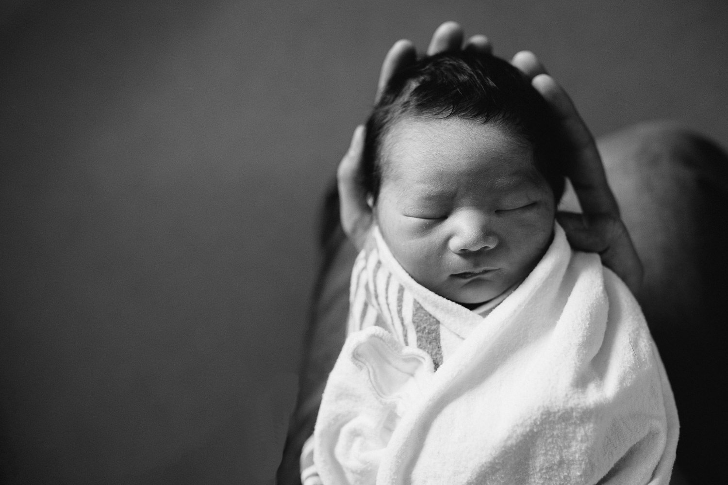 1 day old baby boy lying asleep in dads arms, wrapped in hospital swaddle - Barrie Fresh 48 Photography