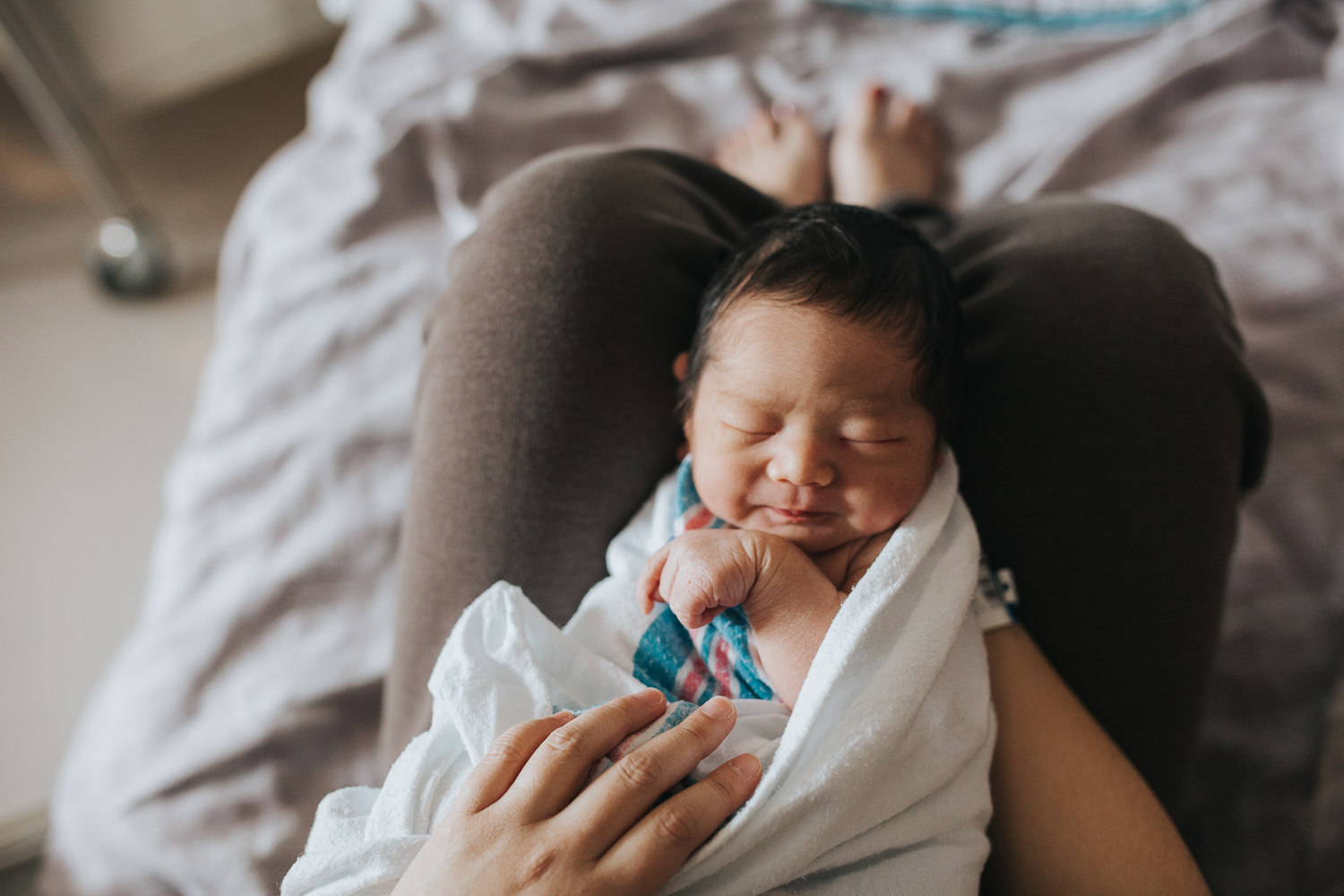 1 day old baby boy in hospital swaddle lying asleep on mom's legs - Markham Lifestyle Photography