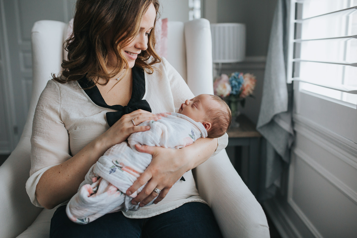 new mom sits in chair holding swaddled, sleeping 2 week old baby girl - Markham Lifestyle Photography