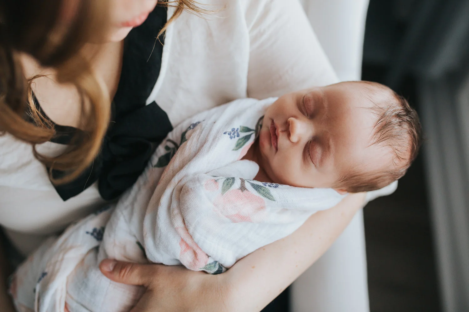 new mom sits in chair holding swaddled, sleeping 2 week old baby girl - Stouffville Lifestyle Photography