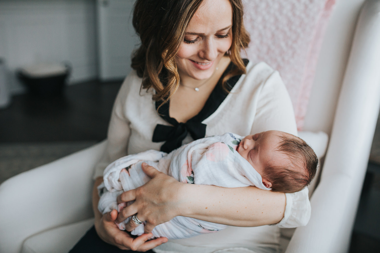 new mom sits in chair holding swaddled, sleeping 2 week old baby girl - Newmarket Lifestyle Photography