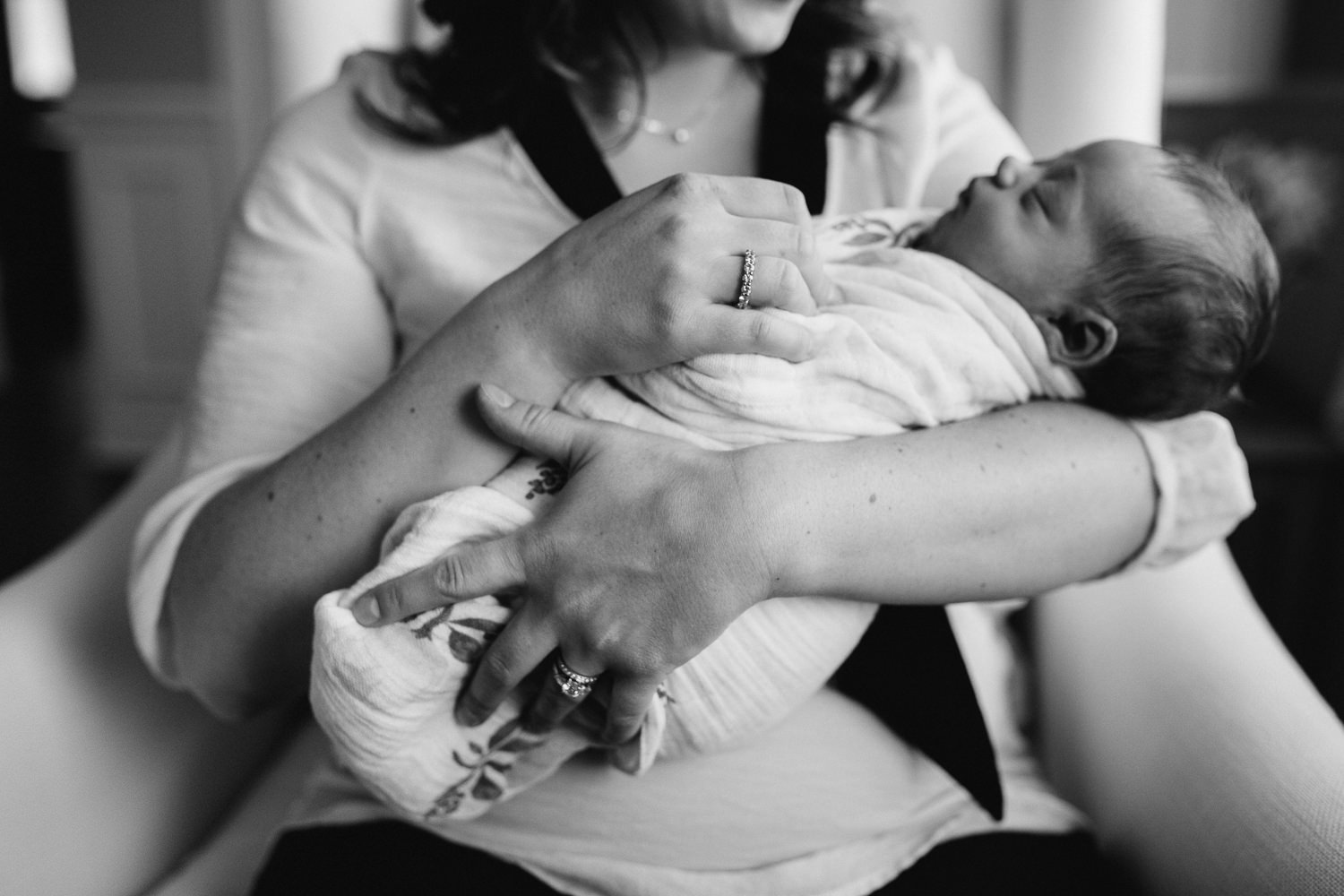 new mom sits in chair holding swaddled, sleeping 2 week old baby girl - Barrie Lifestyle Photography