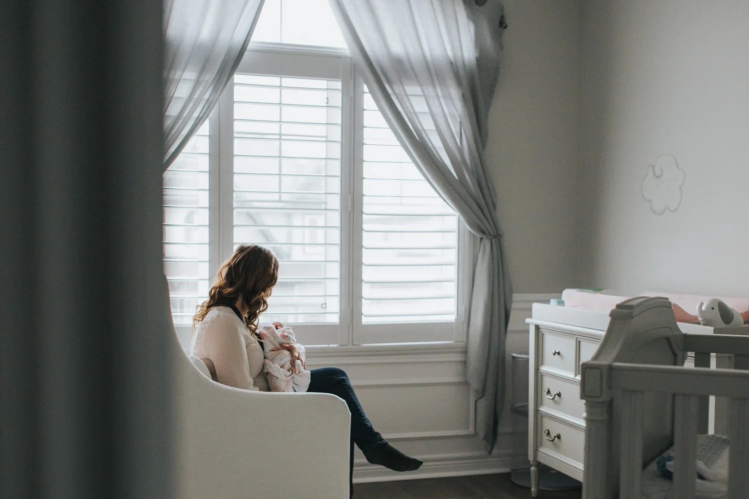 new mom sits in chair holding swaddled, sleeping 2 week old baby girl - Uxbridge Lifestyle Photography