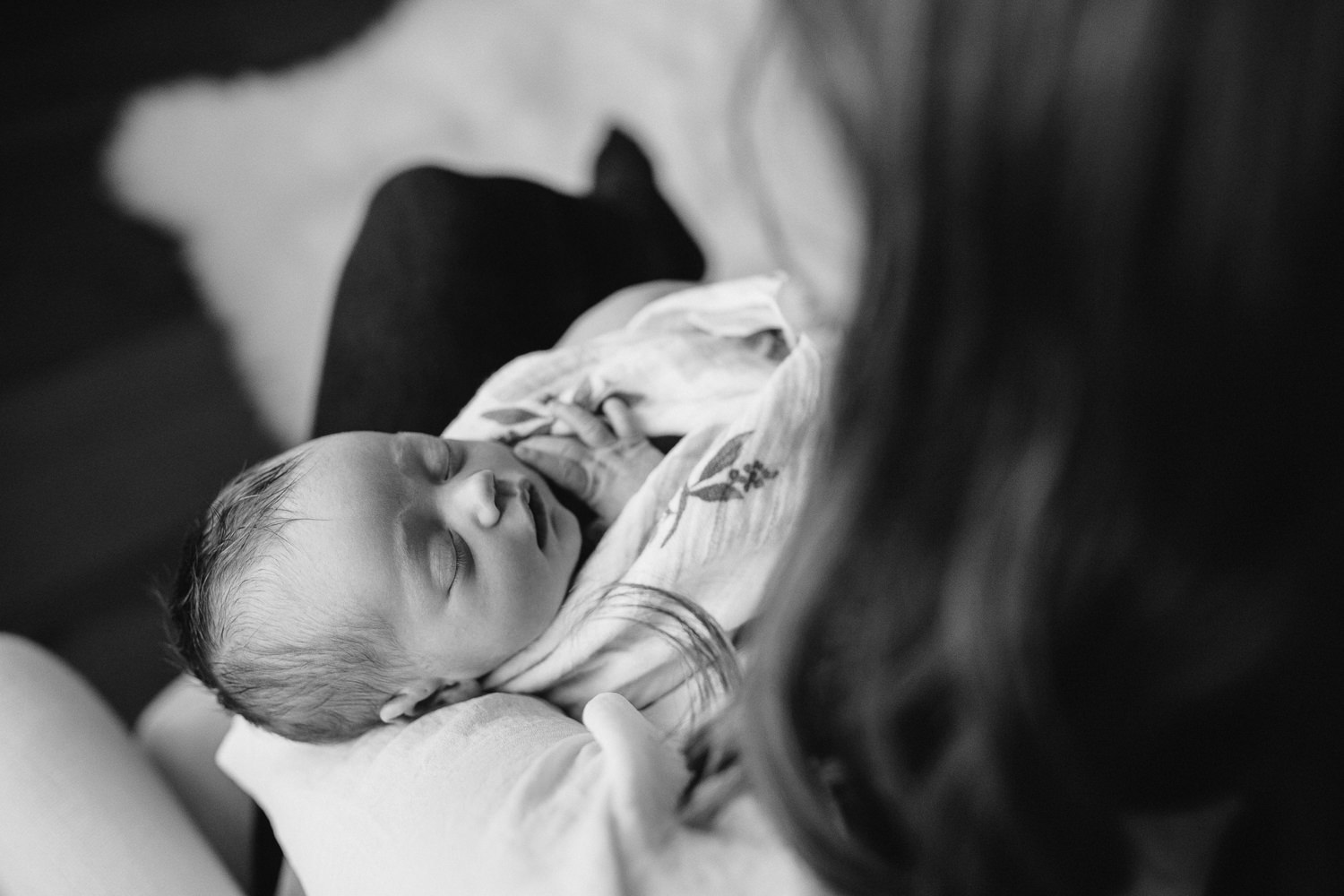 new mom sits in chair holding swaddled, sleeping 2 week old baby girl - Barrie In-Home Photography