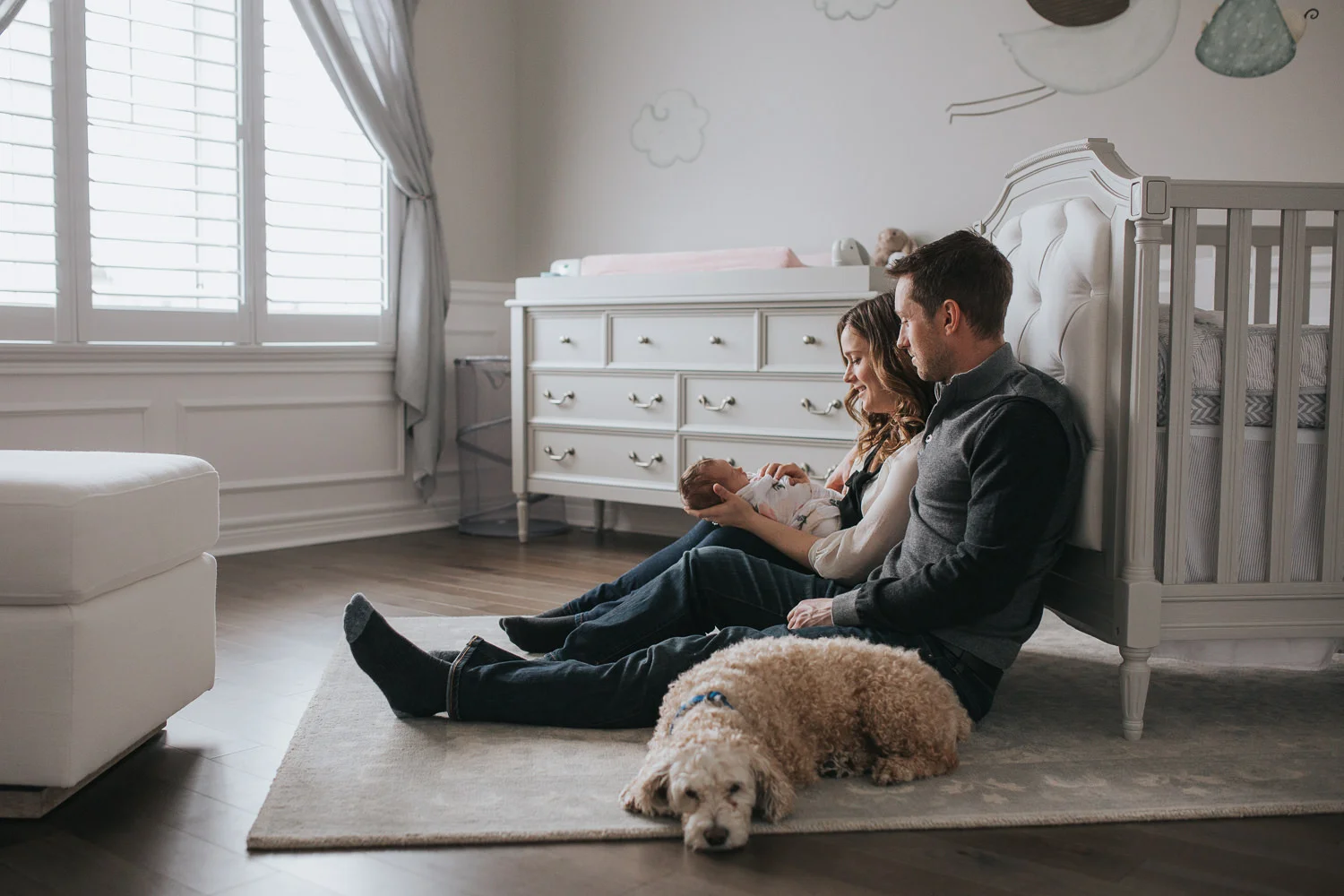 first time parents sitting on nursery floor holding 2 week old baby daughter, family dog looking on - Stouffville Lifestyle Photos