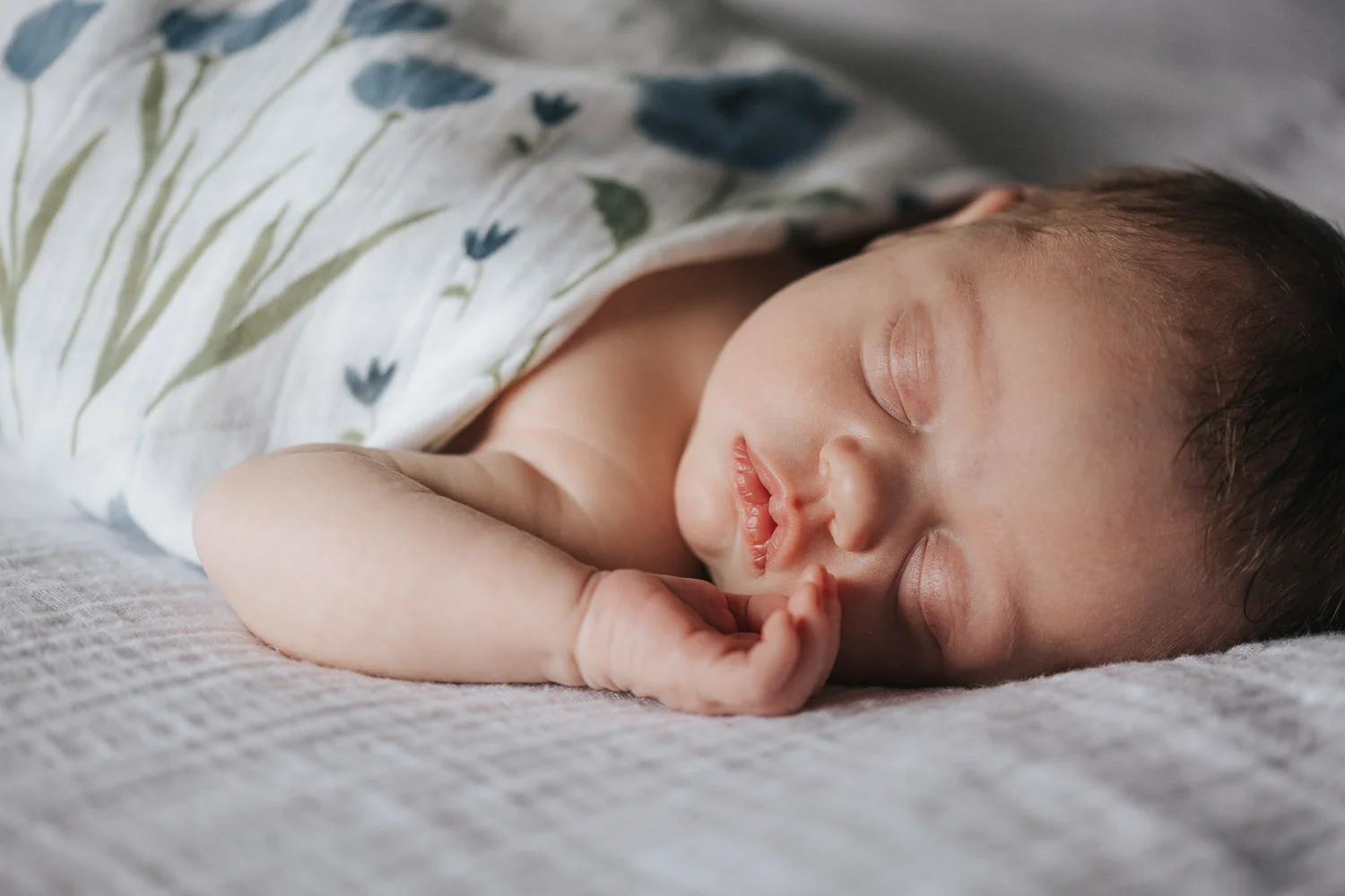 2 week old baby girl in swaddle lying asleep on bed with hands near face - Newmarket In-Home Photos