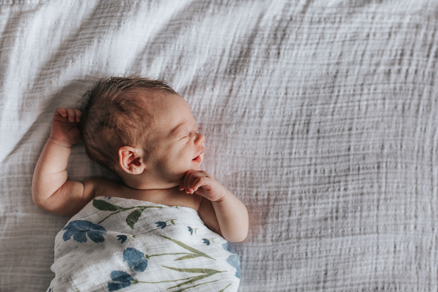 2 week old baby girl in swaddle lying asleep on bed, smiling - Stouffville In-Home