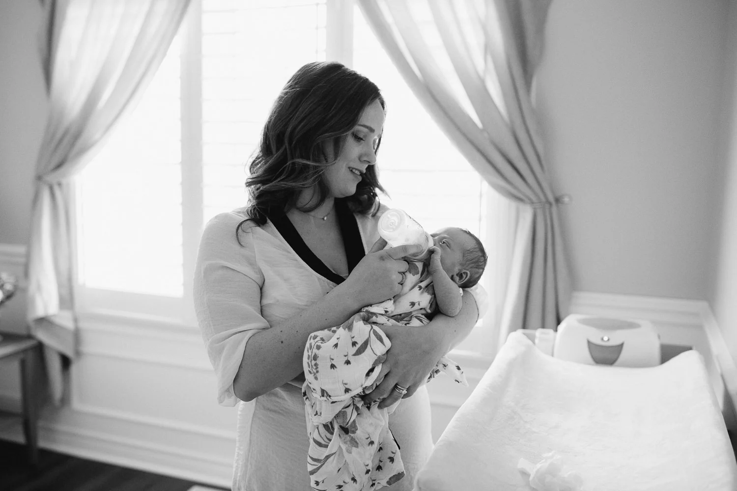 New mom bottle feeding 2 week old baby daughter standing in nursery - Uxbridge In-Home Photos
