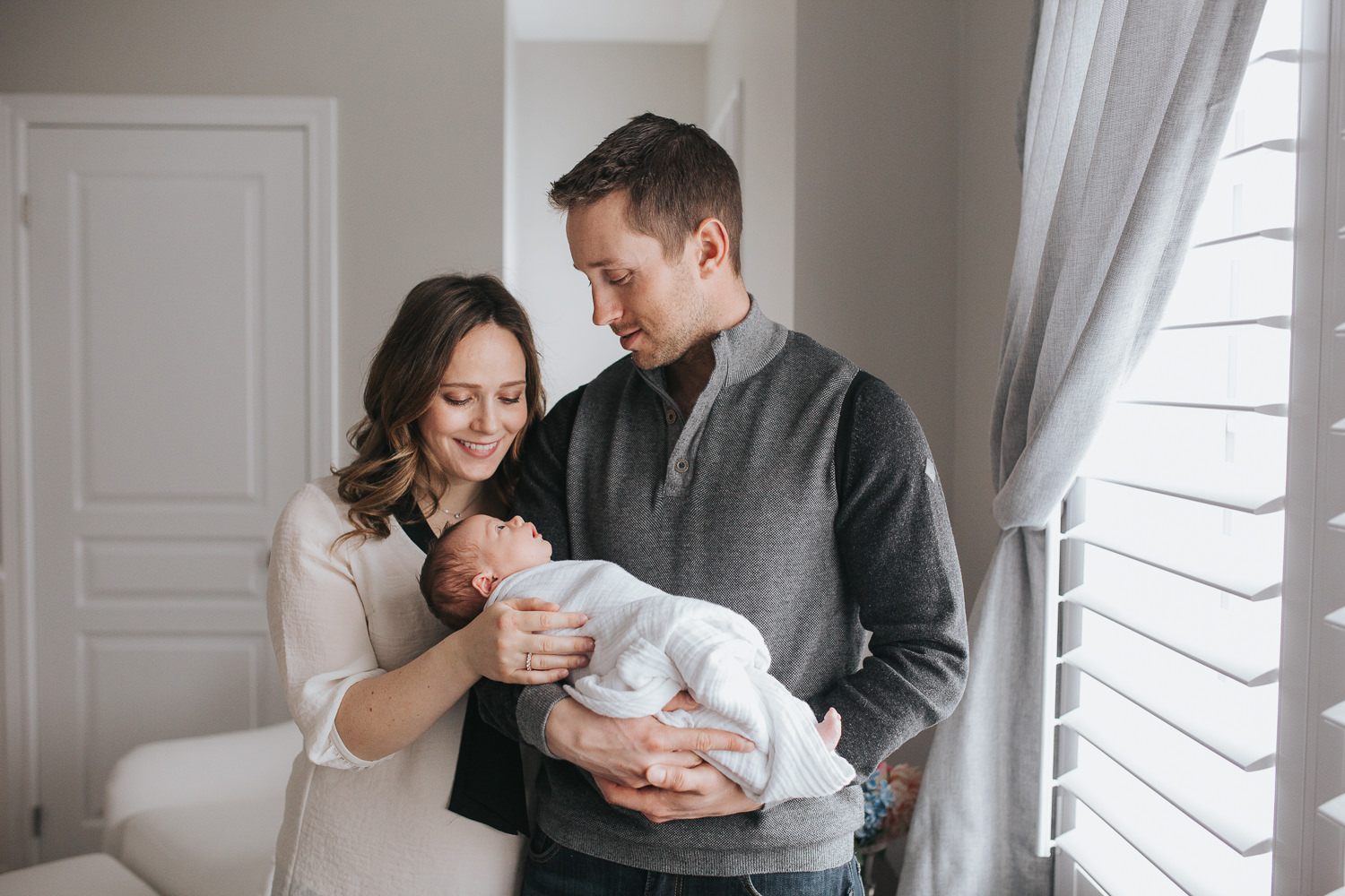 new parents standing in nursery holding and looking at their 2 week old baby girl - Newmarket In-Home Photography