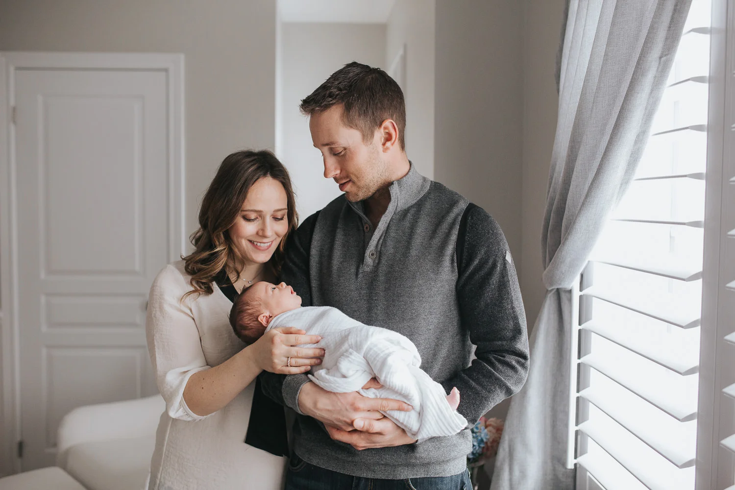 new parents standing in nursery holding and looking at their 2 week old baby girl - Newmarket In-Home Photography