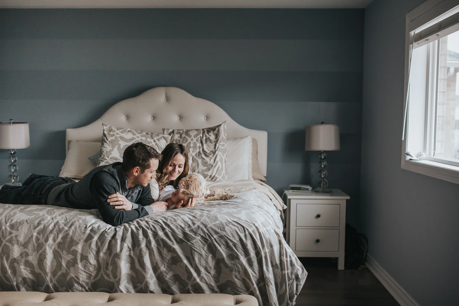 new parents lying on master bed looking at their 2 week old baby girl with family dog - Uxbridge In-Home Photography