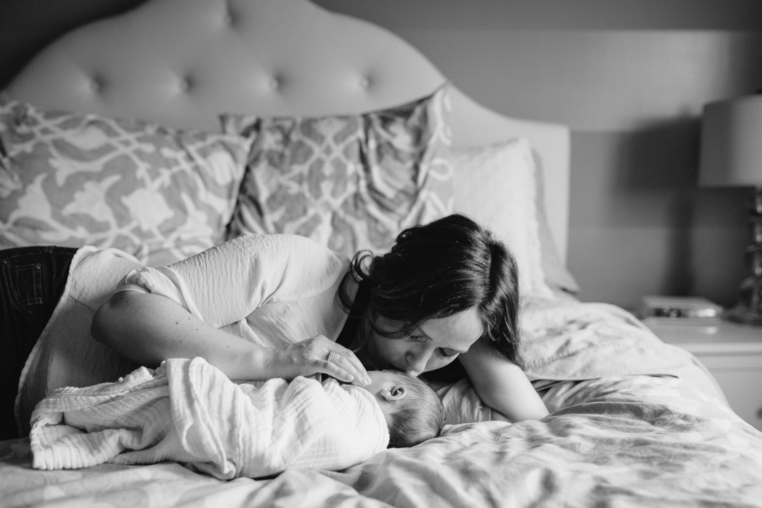 first time mom lying on master bed with 2 week old baby daughter, kissing her on forehead - Markham Lifestyle Photos