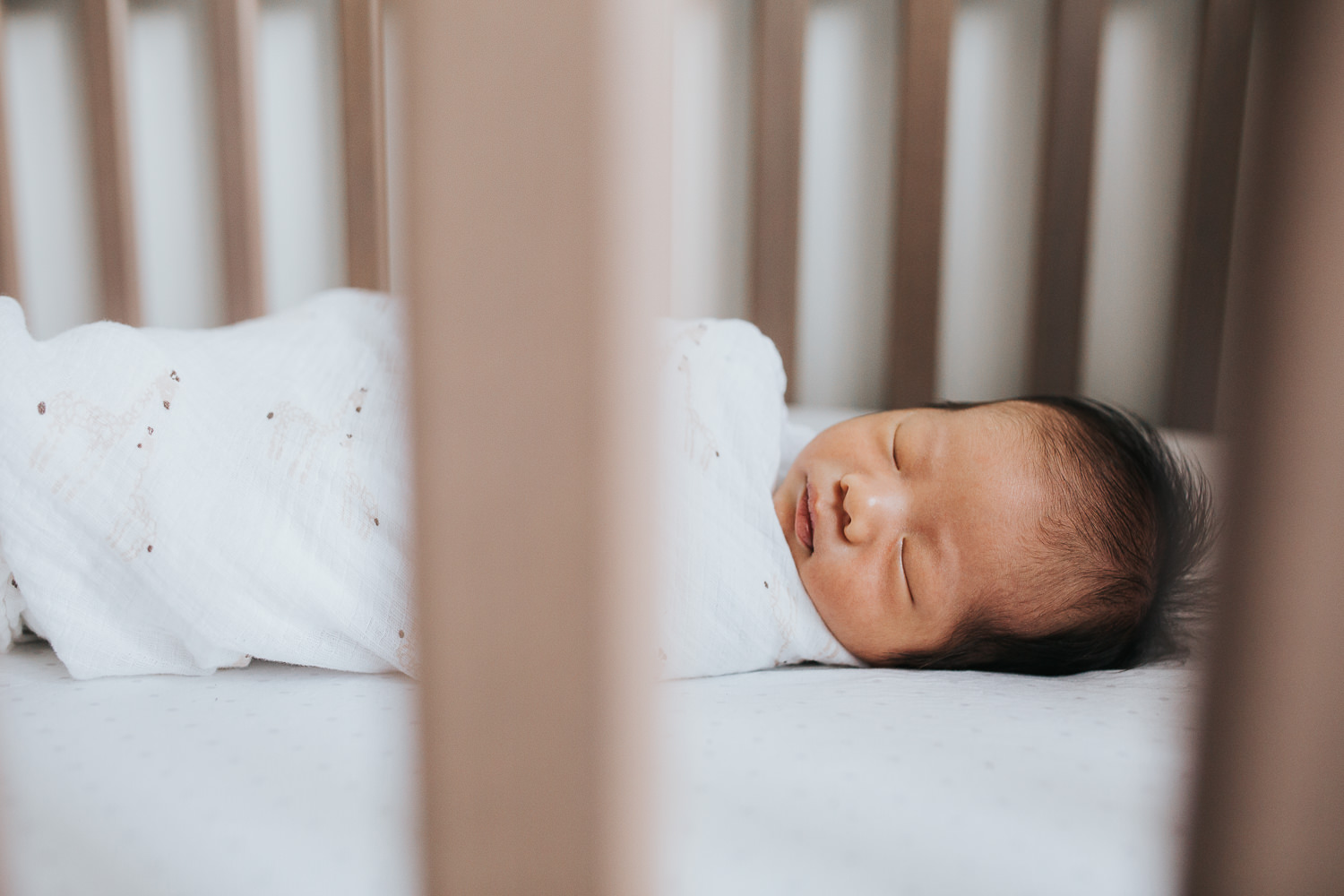 2 week old baby boy with dark hair lying swaddled and sleeping in crib - Uxbridge Lifestyle Photography