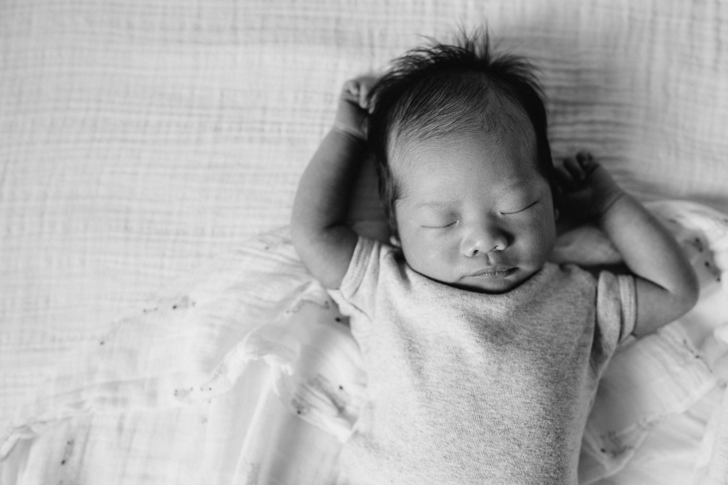 2 week old baby boy lying sleeping on bed with arms above head - Newmarket In-Home Photography