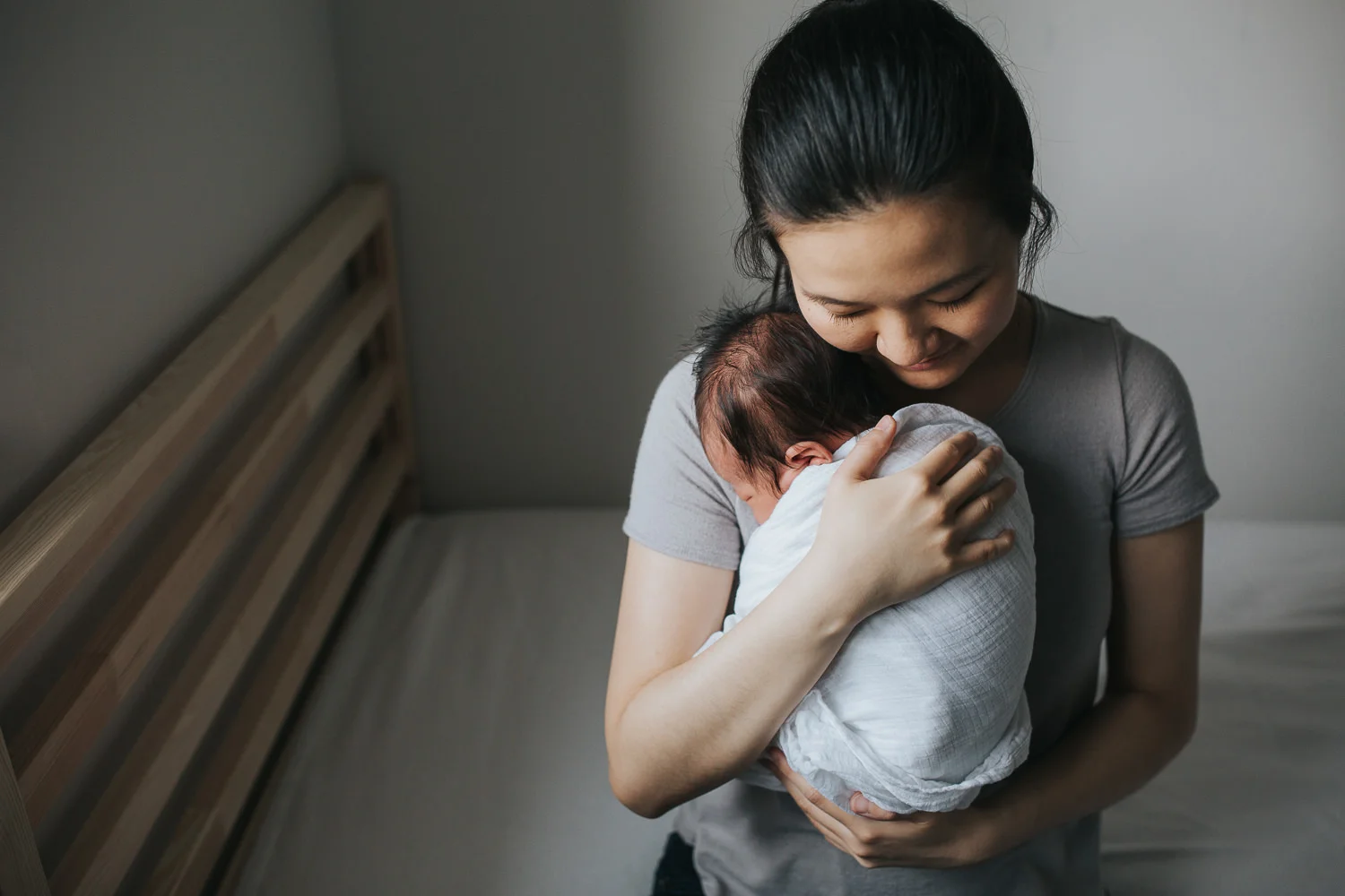 new mother cuddles 2 week old baby son in swaddle to chest - Barrie In-Home Photography