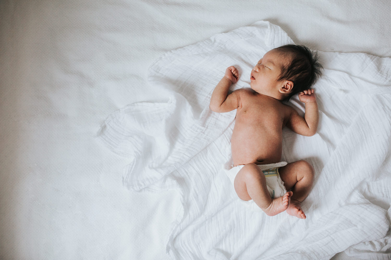 2 week old baby boy with dark hair in diaper, lying asleep on white bed - Uxbridge In-Home Photos