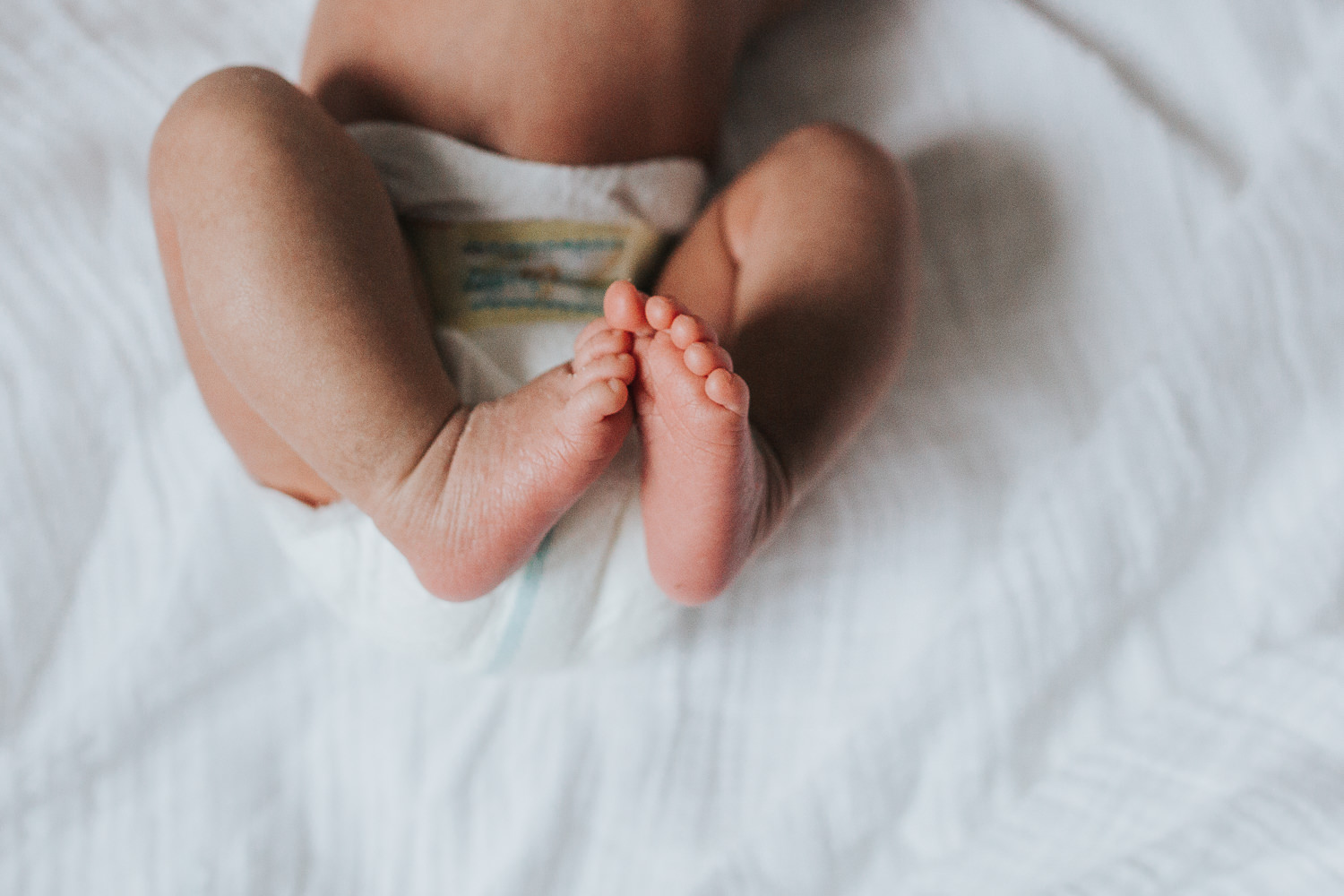 2 week old baby boy in diaper on white bed, close up of feet and toes - Newmarket Lifestyle Photography