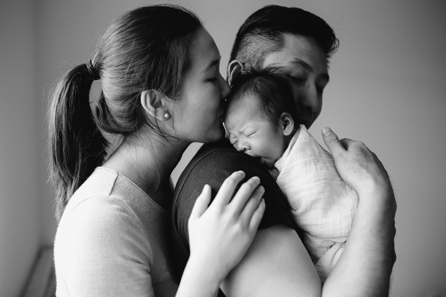 new dad hold 2 week old baby boy over shoulder, mom kisses baby's head - Barrie Lifestyle Photography