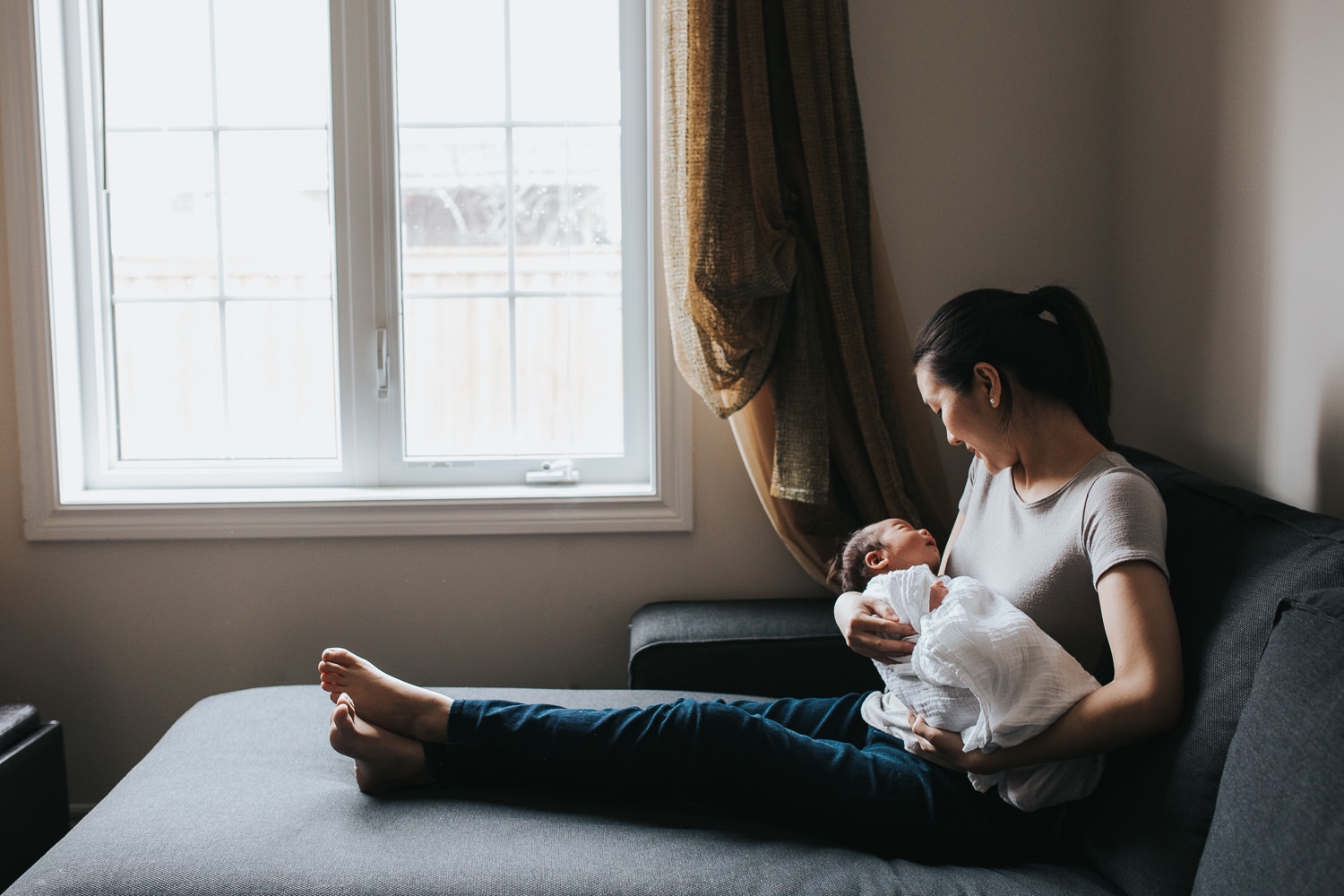 first time mother sitting on couch holding 2 week old baby son - Newmarket In-Home Photography